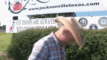 a man in a cowboy hat stands in front of a sign that says " our troops are always welcome "