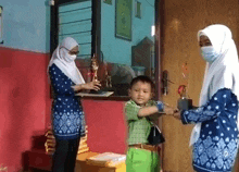 a woman wearing a mask is giving a trophy to a boy