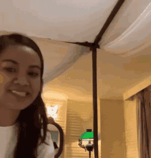 a woman is smiling in a room with a canopy over her head and a lamp .