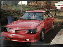 a red car is parked in a driveway with a fence behind it