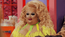 a drag queen with blonde hair and red lips is wearing a yellow and green outfit