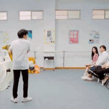 a man in a white shirt stands in front of a rainbow in a room with people sitting on benches