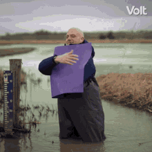 a man is kneeling in a flooded field holding a purple piece of paper in front of a volt sign