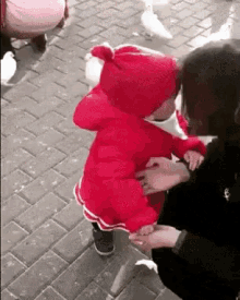 a little girl in a red jacket is walking on a brick sidewalk while a woman holds her hand .