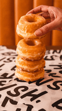 a person is holding a stack of glazed donuts over a table cloth that says ' s ' on it