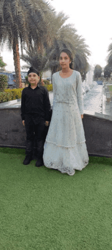 a boy in a black shirt and a girl in a white dress are posing for a picture in front of a fountain .