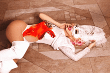 a woman laying on the floor wearing a white bodysuit and feathers