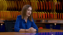 a woman in a blue shirt is sitting at a table with her hands folded and a glass of water .