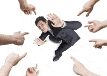 a man in a suit is surrounded by fingers pointing to him