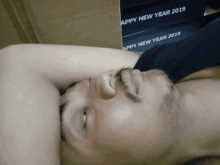 a man with a beard is laying down in front of a stack of boxes that say happy new year 2019