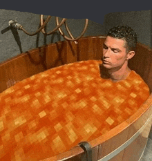 a man is taking a bath in a wooden bathtub filled with orange liquid .