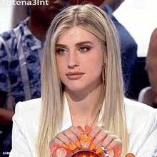 a woman with long blonde hair is sitting in front of a group of people and holding a bowl of candy .