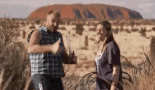 a man and a woman are standing next to each other in a field in front of a mountain .