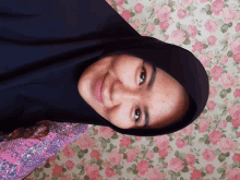 a woman wearing a black hijab is smiling in front of a floral wall