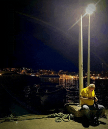 a man in a yellow shirt sits on a dock at night looking at his phone