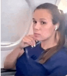 a woman is sitting on an airplane wearing ear buds and looking out the window .