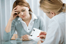 a woman is sitting at a table with a glass of water and a clipboard while a doctor writes on it .