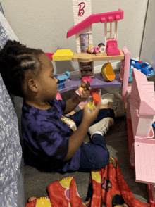 a little girl sits on the floor playing with a barbie house