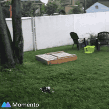 a backyard with a sandbox and a momento logo on the bottom