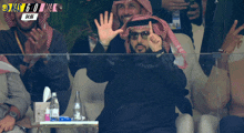 a man in a keffiyeh waves his hand in front of a scoreboard that says ' king ' on it