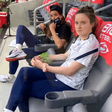 two women sitting in a stadium with a big steel blanket on the back of their seats