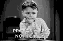 a black and white photo of a young boy sitting at a desk with his hand on his chin and probably best not to move .