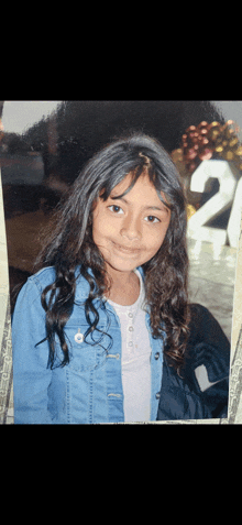 a young girl in a denim jacket is standing in front of a 21 sign