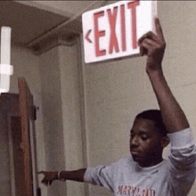 a man in a maryland shirt is holding up a red exit sign