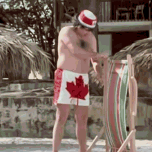 a shirtless man wearing a hat and a pair of canadian shorts is standing next to a beach chair .