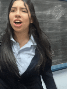 a girl in a school uniform stands in front of a blackboard with her mouth open