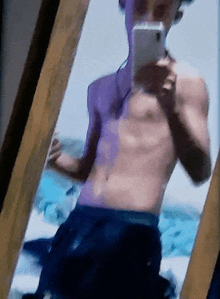 a shirtless man is taking a selfie in front of a mirror with his phone .