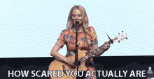 a woman singing into a microphone while holding a guitar with the words " how scared you actually are " behind her