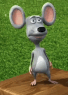 a cartoon mouse is standing on a wooden table in front of a grassy field .