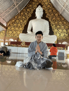 a man is kneeling in front of a statue of buddha