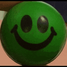 a green smiley face with black eyes is being held in someone 's hand