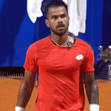 a man wearing a red shirt with a lotto logo on the front is standing on a tennis court .