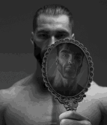 a shirtless man is holding a mirror with a picture of himself on it