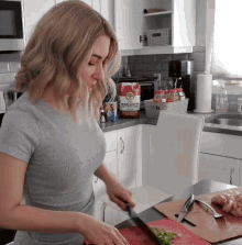 a woman in a grey shirt is cutting vegetables in a kitchen with a bag of beans on the counter