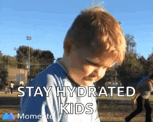 a young boy is standing in a park with the words `` stay hydrated kids '' written above him .