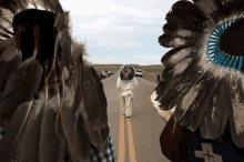 a man wearing a feathered headdress is walking down a road .