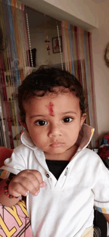 a young boy with a red dot on his forehead looks at the camera