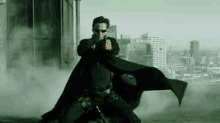 a man in a black cape is holding a gun in front of a city skyline .