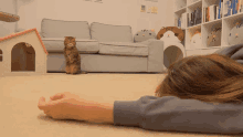 a woman laying on the floor with a cat standing in the background