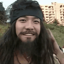 a man with long hair and a beard is wearing a black headband and smiling .