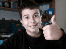 a young boy giving a thumbs up in front of a bookshelf