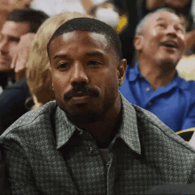 a man with a beard is sitting in a crowd and looking at something