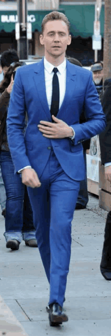 a man in a blue suit and black tie is walking down a sidewalk