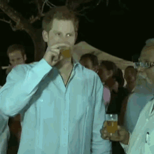 a man in a blue shirt is drinking from a glass while another man holds a glass of beer .