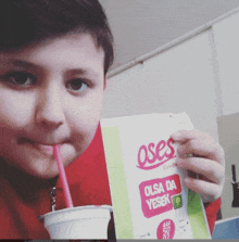 a young boy drinking from a cup with a straw while holding a package of oses