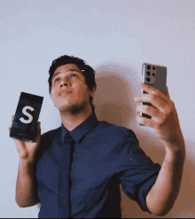 a man in a blue shirt and tie is holding up a phone and a box with the letter s on it